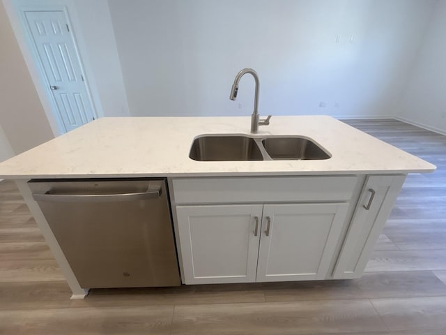 kitchen with light wood-type flooring, a sink, light stone counters, stainless steel dishwasher, and white cabinetry