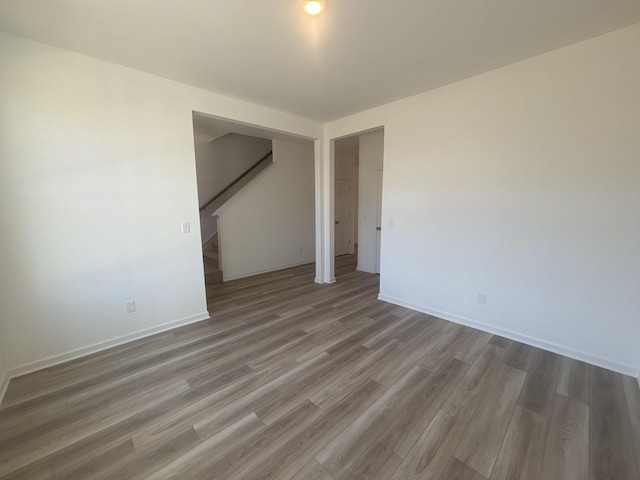 unfurnished room with stairs, baseboards, and wood finished floors