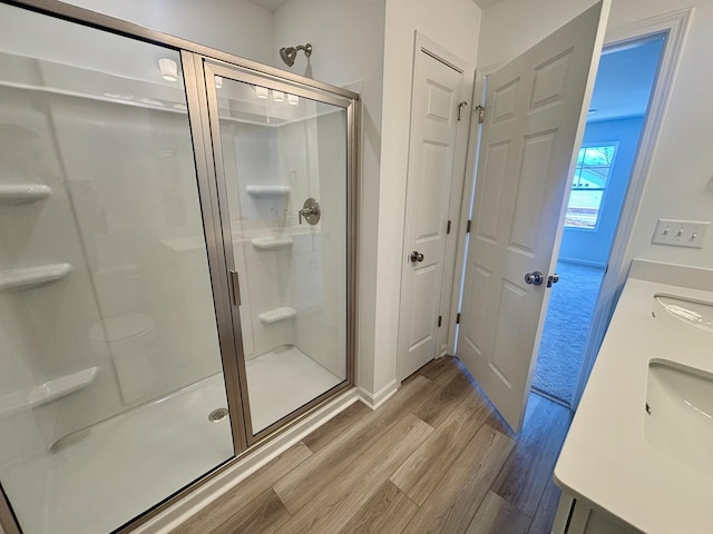 bathroom featuring baseboards, wood finished floors, a stall shower, and vanity