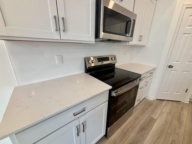 kitchen featuring backsplash, appliances with stainless steel finishes, white cabinets, and light wood-style flooring