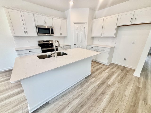 kitchen featuring a center island with sink, a sink, stainless steel appliances, light wood-style floors, and white cabinets