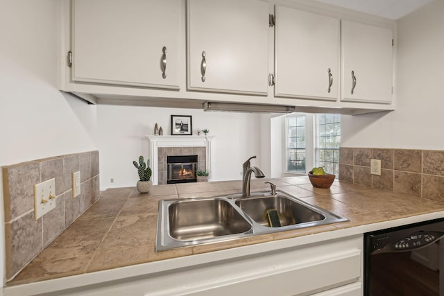 kitchen featuring black dishwasher, a tile fireplace, a sink, and white cabinets