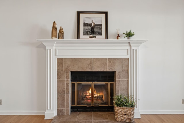 details with baseboards, a tiled fireplace, and wood finished floors