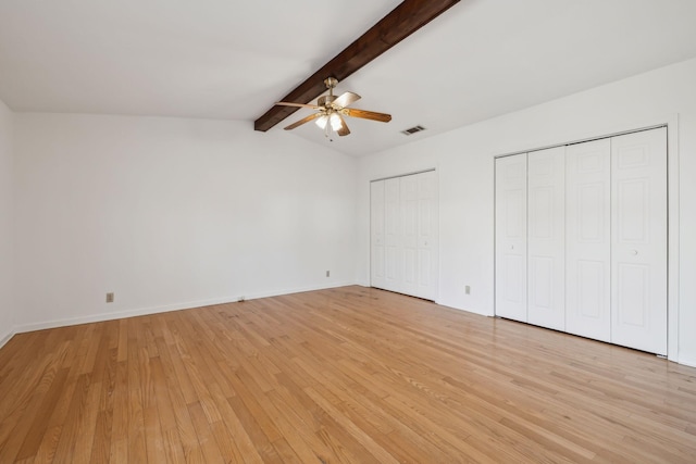 unfurnished bedroom featuring lofted ceiling with beams, light wood-style flooring, visible vents, baseboards, and two closets