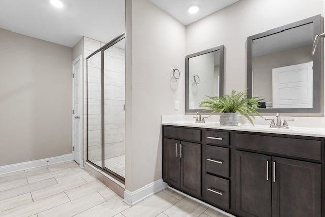 full bathroom featuring baseboards, double vanity, a sink, and a shower stall