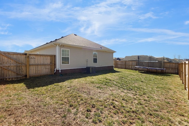 back of house with a trampoline, a fenced backyard, a lawn, and central AC