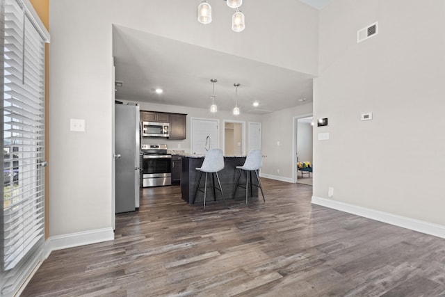 kitchen featuring baseboards, visible vents, appliances with stainless steel finishes, a breakfast bar, and dark wood-type flooring