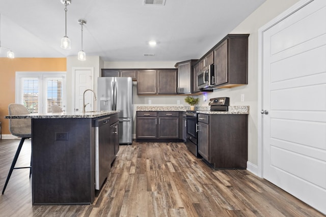 kitchen with dark wood finished floors, appliances with stainless steel finishes, a sink, dark brown cabinets, and light stone countertops