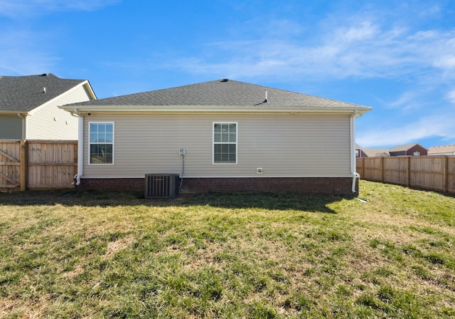 rear view of property featuring a fenced backyard, a shingled roof, central AC, and a yard