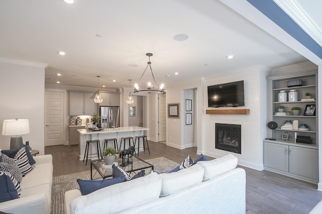 living area featuring a large fireplace, recessed lighting, wood finished floors, and crown molding