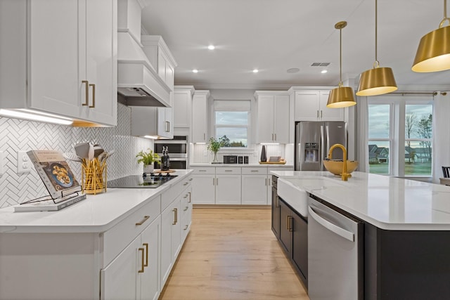 kitchen featuring appliances with stainless steel finishes, light countertops, an island with sink, and custom exhaust hood