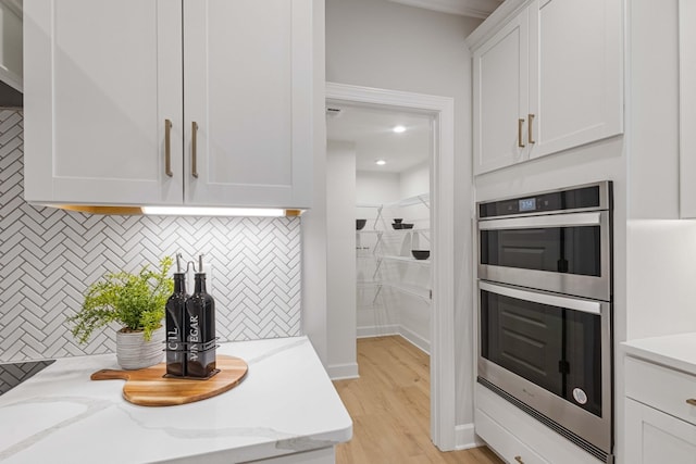 kitchen featuring tasteful backsplash, white cabinets, light stone countertops, light wood-style floors, and double oven