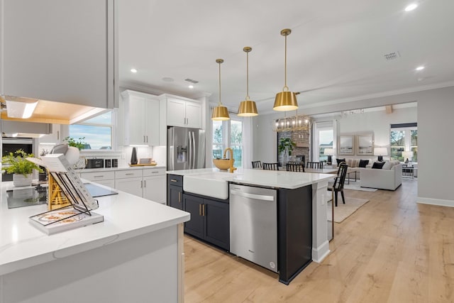 kitchen with appliances with stainless steel finishes, ornamental molding, open floor plan, white cabinets, and a sink