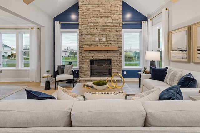 living room featuring lofted ceiling, a stone fireplace, wood finished floors, and baseboards