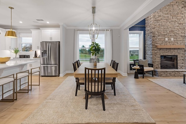 dining area with a healthy amount of sunlight, light wood-style floors, crown molding, and a stone fireplace