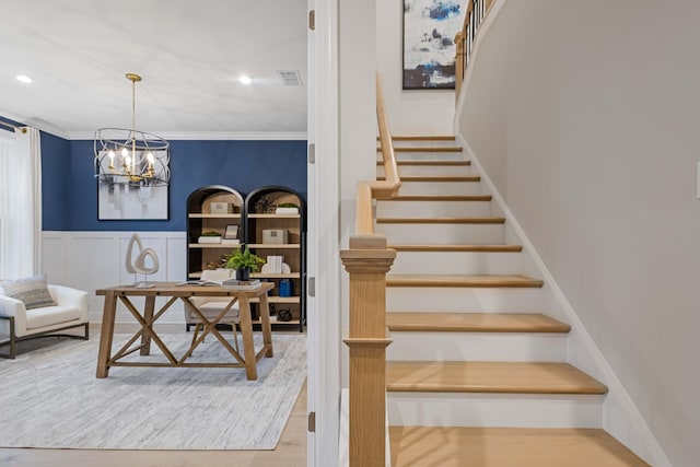 stairs featuring visible vents, wainscoting, ornamental molding, wood finished floors, and a chandelier