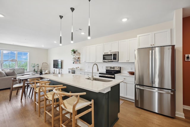 kitchen featuring wood finished floors, a sink, white cabinets, appliances with stainless steel finishes, and backsplash