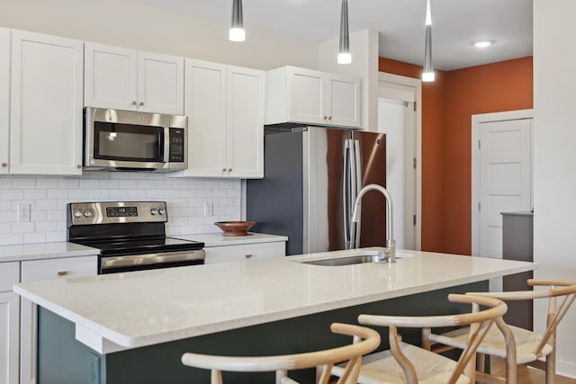 kitchen featuring a breakfast bar area, decorative backsplash, appliances with stainless steel finishes, white cabinetry, and a sink