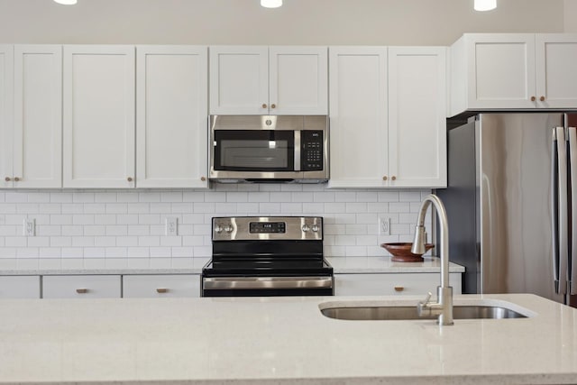 kitchen with stainless steel appliances, tasteful backsplash, white cabinetry, a sink, and light stone countertops