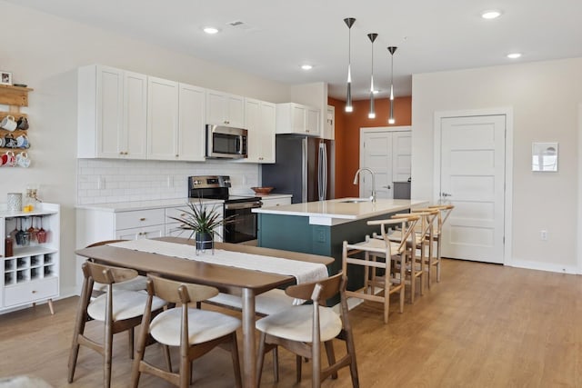 kitchen featuring light wood-style flooring, appliances with stainless steel finishes, decorative backsplash, and a sink