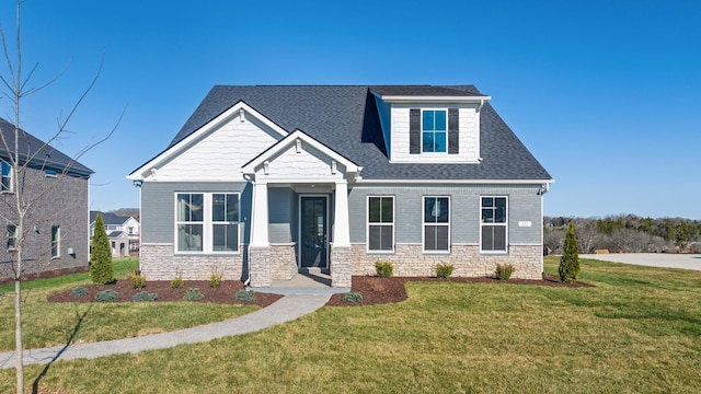 craftsman inspired home with a shingled roof, a front yard, and stone siding