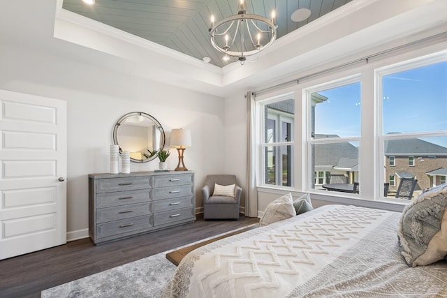 bedroom with an inviting chandelier, ornamental molding, a raised ceiling, and dark wood-style flooring