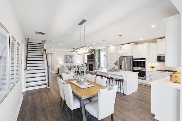 dining area with stairs, visible vents, a fireplace with raised hearth, and dark wood finished floors