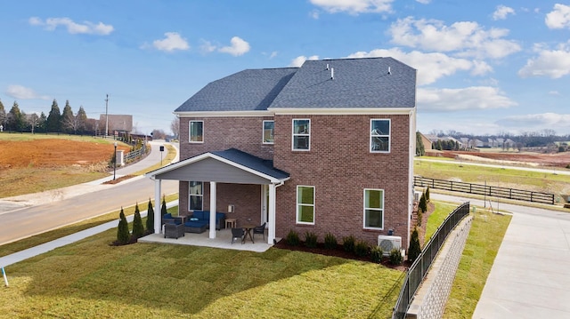 rear view of property with a yard, brick siding, fence, and roof with shingles