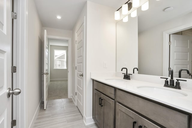 bathroom with double vanity, baseboards, a sink, and recessed lighting