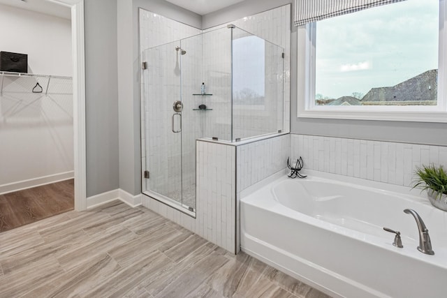 bathroom with a garden tub, a shower stall, a walk in closet, and baseboards