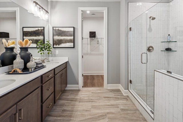 full bath with a sink, baseboards, a spacious closet, a shower stall, and double vanity