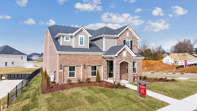 view of front of home with roof with shingles, brick siding, board and batten siding, a front yard, and fence