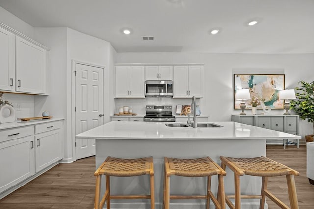 kitchen with decorative backsplash, dark wood finished floors, appliances with stainless steel finishes, a breakfast bar, and a sink