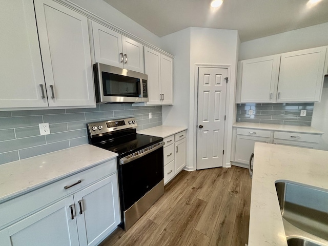 kitchen with backsplash, light stone counters, appliances with stainless steel finishes, wood finished floors, and white cabinetry