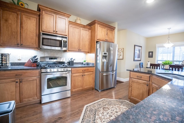 kitchen with dark wood-style floors, appliances with stainless steel finishes, brown cabinets, pendant lighting, and a sink