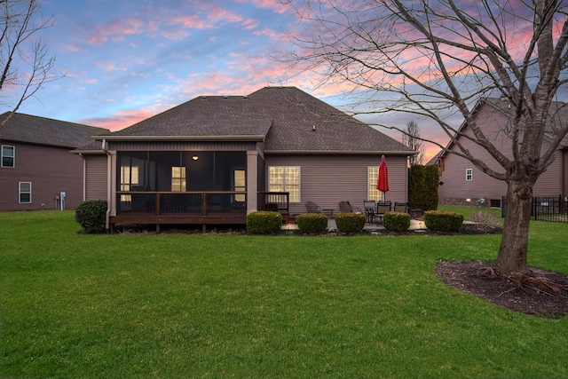 back of property at dusk with a shingled roof, a sunroom, a patio area, and a yard