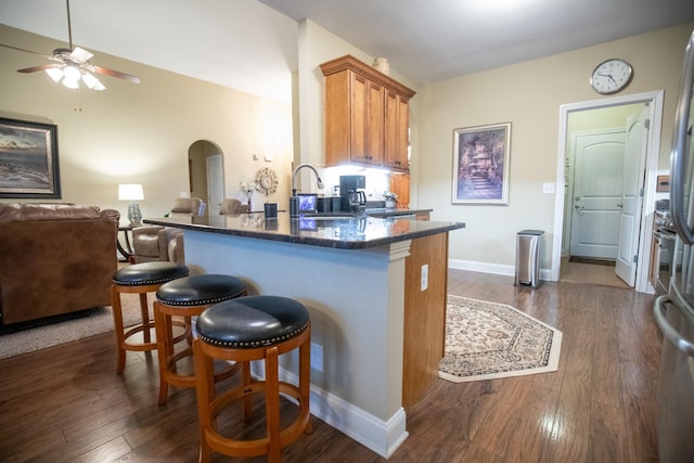 kitchen with arched walkways, a peninsula, a kitchen breakfast bar, brown cabinets, and dark wood-style floors