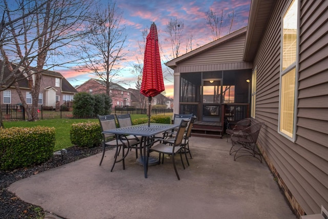 patio terrace at dusk featuring a sunroom, fence, and outdoor dining area