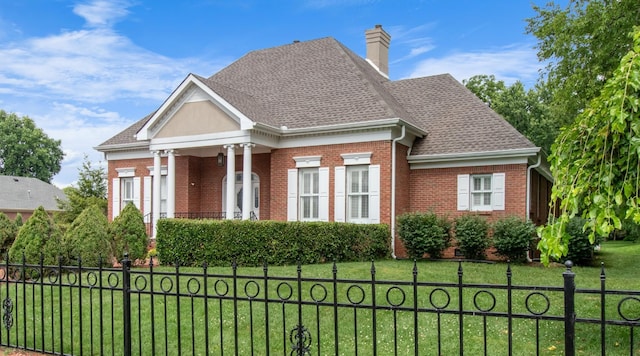 neoclassical home with a fenced front yard, brick siding, roof with shingles, a chimney, and a front yard