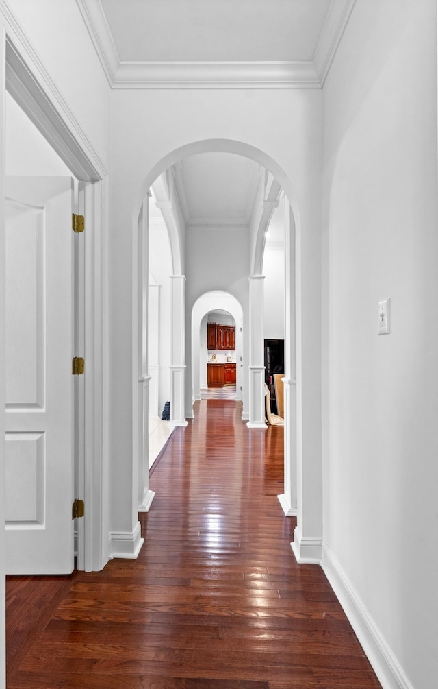 corridor featuring wood-type flooring, baseboards, arched walkways, and crown molding