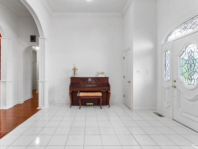 foyer with baseboards, arched walkways, a high ceiling, crown molding, and light tile patterned flooring