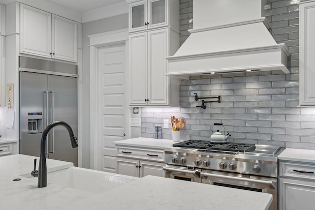 kitchen with custom range hood, glass insert cabinets, white cabinets, a sink, and high quality appliances