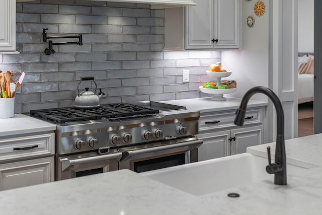 kitchen with range with two ovens, light stone counters, backsplash, white cabinetry, and a sink