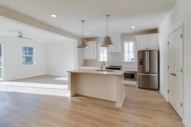 kitchen with stainless steel appliances, a sink, white cabinets, light wood-type flooring, and backsplash