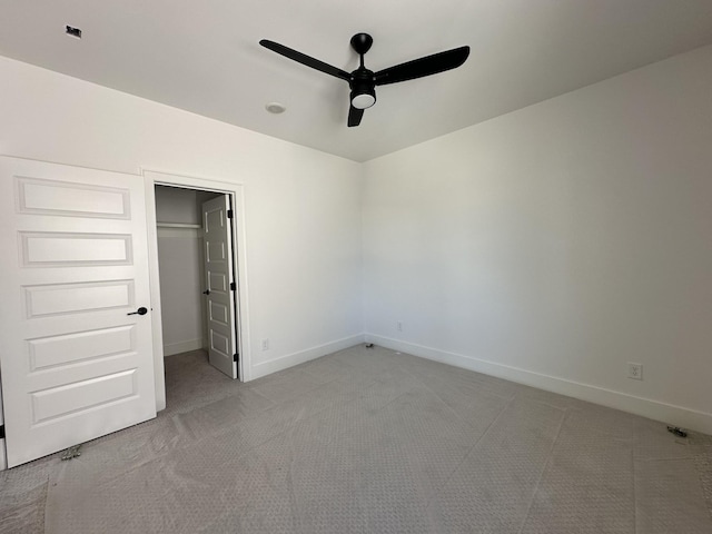 unfurnished bedroom with ceiling fan, light colored carpet, baseboards, a closet, and a walk in closet