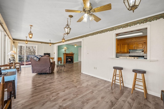 living area with baseboards, a lit fireplace, a ceiling fan, and wood finished floors