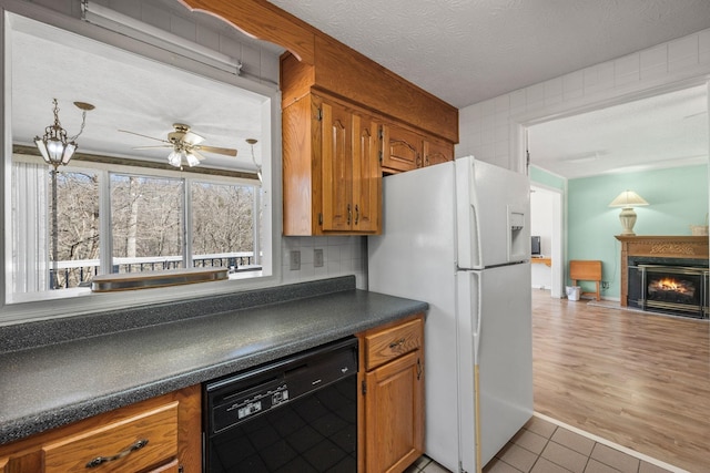 kitchen with freestanding refrigerator, brown cabinets, dishwasher, and dark countertops