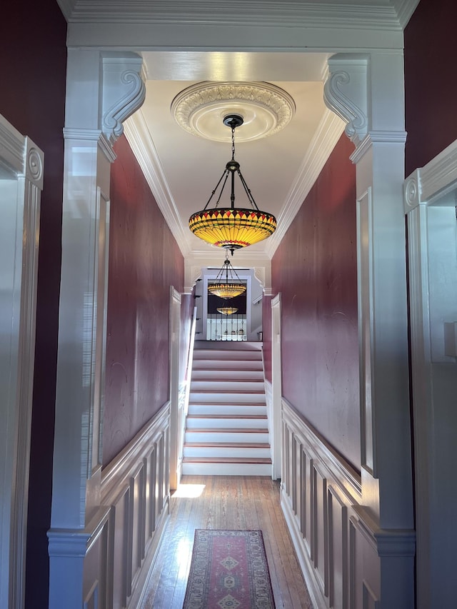 hall with crown molding, wood-type flooring, a decorative wall, stairway, and ornate columns