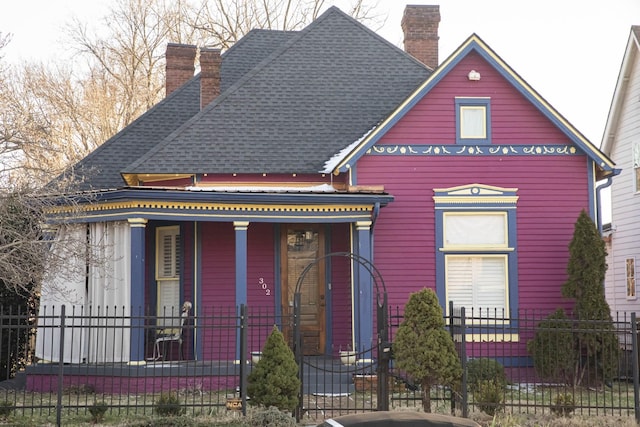 view of front of property featuring covered porch, roof with shingles, a chimney, and a fenced front yard