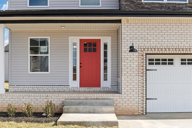 view of exterior entry featuring a garage and brick siding